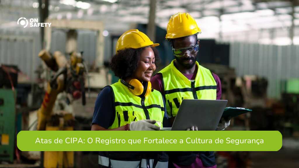 Dois trabalhadores usando equipamentos de segurança, como capacetes e coletes refletivos, estão revisando informações em um laptop dentro de um ambiente industrial. A imagem acompanha o título "Atas de CIPA: O Registro que Fortalece a Cultura de Segurança"