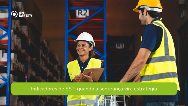 Dois profissionais em um armazém conversam enquanto vestem coletes de alta visibilidade e capacetes de segurança. A mulher segura uma prancheta e sorri para o colega, demonstrando um ambiente colaborativo. Estantes cheias de caixas estão ao fundo. No canto superior esquerdo, está o logo da OnSafety. Na parte inferior da imagem, uma faixa verde exibe o texto: "Indicadores de SST: quando a segurança vira estratégia".