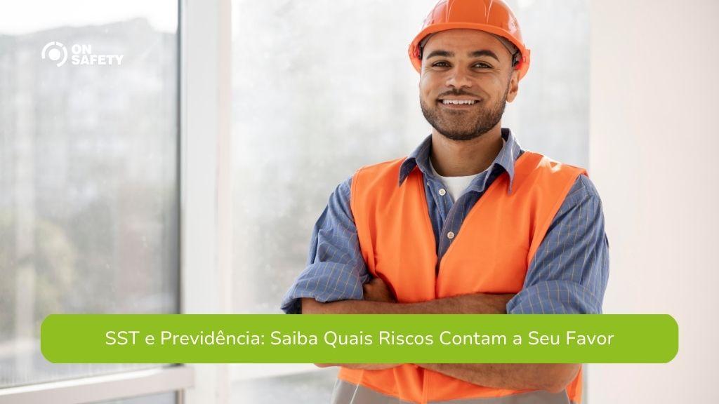 Homem jovem, sorrindo, usando capacete de segurança laranja e colete refletivo laranja sobre uma camisa azul, com os braços cruzados, posando em um ambiente claro com janelas ao fundo. Na parte inferior, uma faixa verde com o texto "SST e Previdência: Saiba Quais Riscos Contam a Seu Favor".