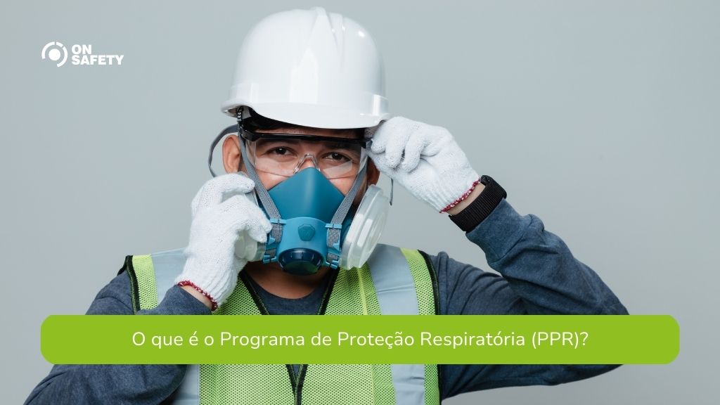 Trabalhador usando capacete de segurança branco, óculos de proteção transparentes e uma máscara respiratória azul, segurando as alças da máscara com as mãos cobertas por luvas de trabalho brancas. Na parte inferior, uma faixa verde com o texto "O que é o Programa de Proteção Respiratória (PPR)?".