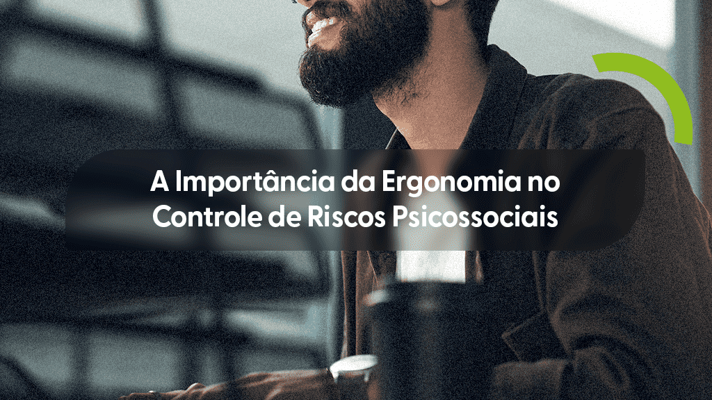 Homem barbudo, sorrindo, sentado em uma mesa de trabalho, olhando para cima e para a direita, com iluminação de fundo. Ele usa óculos e uma camisa escura. Uma forma circular verde estilizada está no canto superior direito. Sobre a imagem, uma caixa de texto cinza transparente com o título "A Importância da Ergonomia no Controle de Riscos Psicossociais".