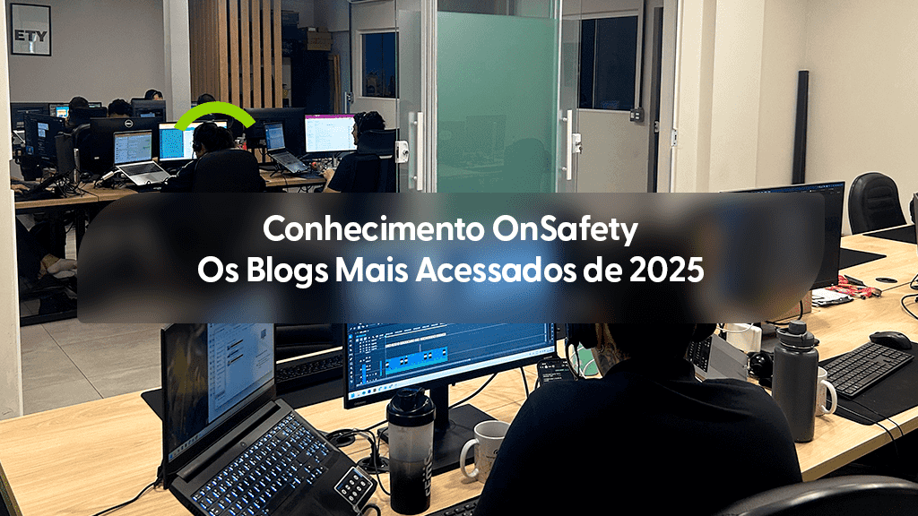 Vista interna de um escritório contemporâneo onde diversos profissionais trabalham em mesas equipadas com notebooks e múltiplos monitores. Em primeiro plano, a parte posterior de um colaborador focado em suas telas de trabalho. Uma forma circular verde estilizada aparece acima de um dos monitores ao fundo. Sobre a imagem, uma caixa de texto cinza transparente contém o título: "Conhecimento OnSafety Os Blogs Mais Acessados de 2025".