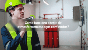 Imagem de um trabalhador em um ambiente industrial, vestindo uniforme azul escuro e um colete refletivo verde-limão. Ele utiliza um capacete de segurança verde com uma lanterna acoplada na lateral e segura outra lanterna manual, apontando-a para a frente enquanto olha atentamente na mesma direção. Ao fundo, são visíveis cilindros vermelhos e painéis de controle. Um pequeno arco verde estilizado aparece logo acima da lanterna manual. No centro, uma faixa cinza transparente destaca o título em branco: "Como funciona o teste de atmosfera em espaços confinados?".